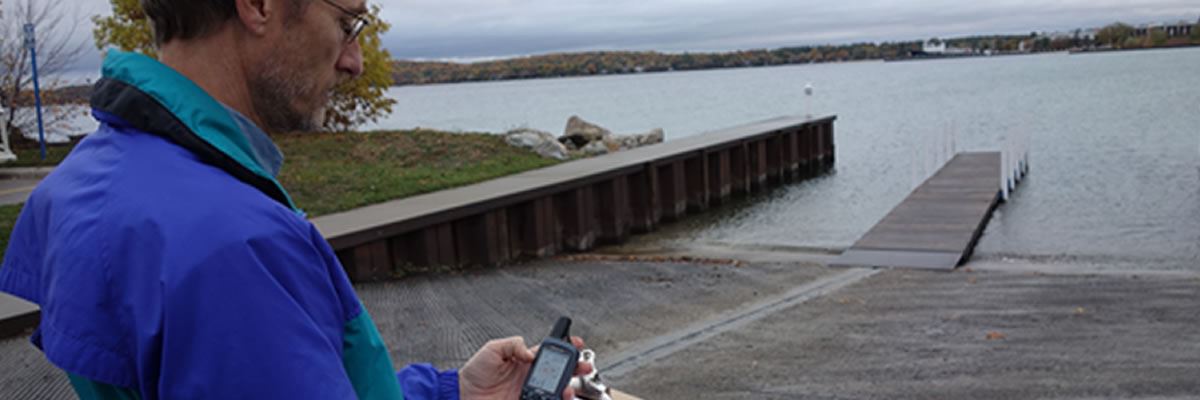 A person with a GPS unit and clipboard stands on a lake shore