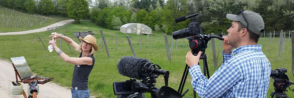 A videographer runs a camera while the subject discusses their topic in an apple orchard