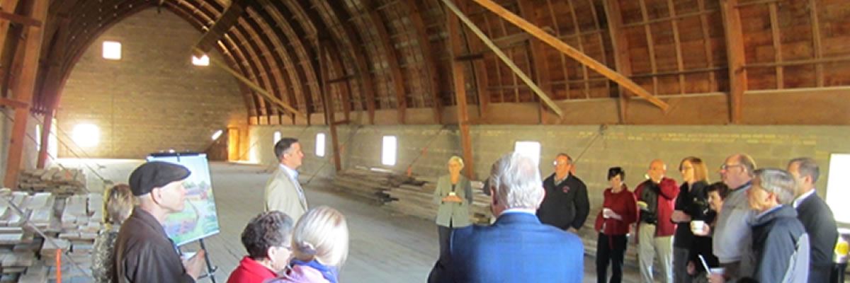 A group listens to a presentation inside a large barn
